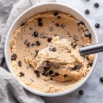 Close-up of creamy cottage cheese cookie dough topped with chocolate chips on parchment paper.