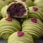 The Best No-Bake Grinch Oreo Truffles – Festive Christmas Treats & Holiday Snacks 4 Top view of green No-Bake Grinch Oreo truffles with festive red icing hats on a parchment-lined tray