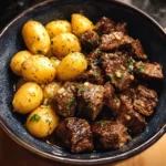 Slow Cooker Garlic Butter Beef Bites with Potatoes served in a bowl, topped with fresh herbs.