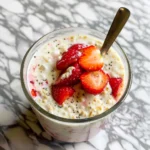 Strawberry cheesecake overnight oats in a mason jar with fresh strawberries and honey drizzle.